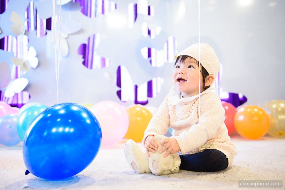 baby girl holding her foot looking up. butterflies and balloons background.